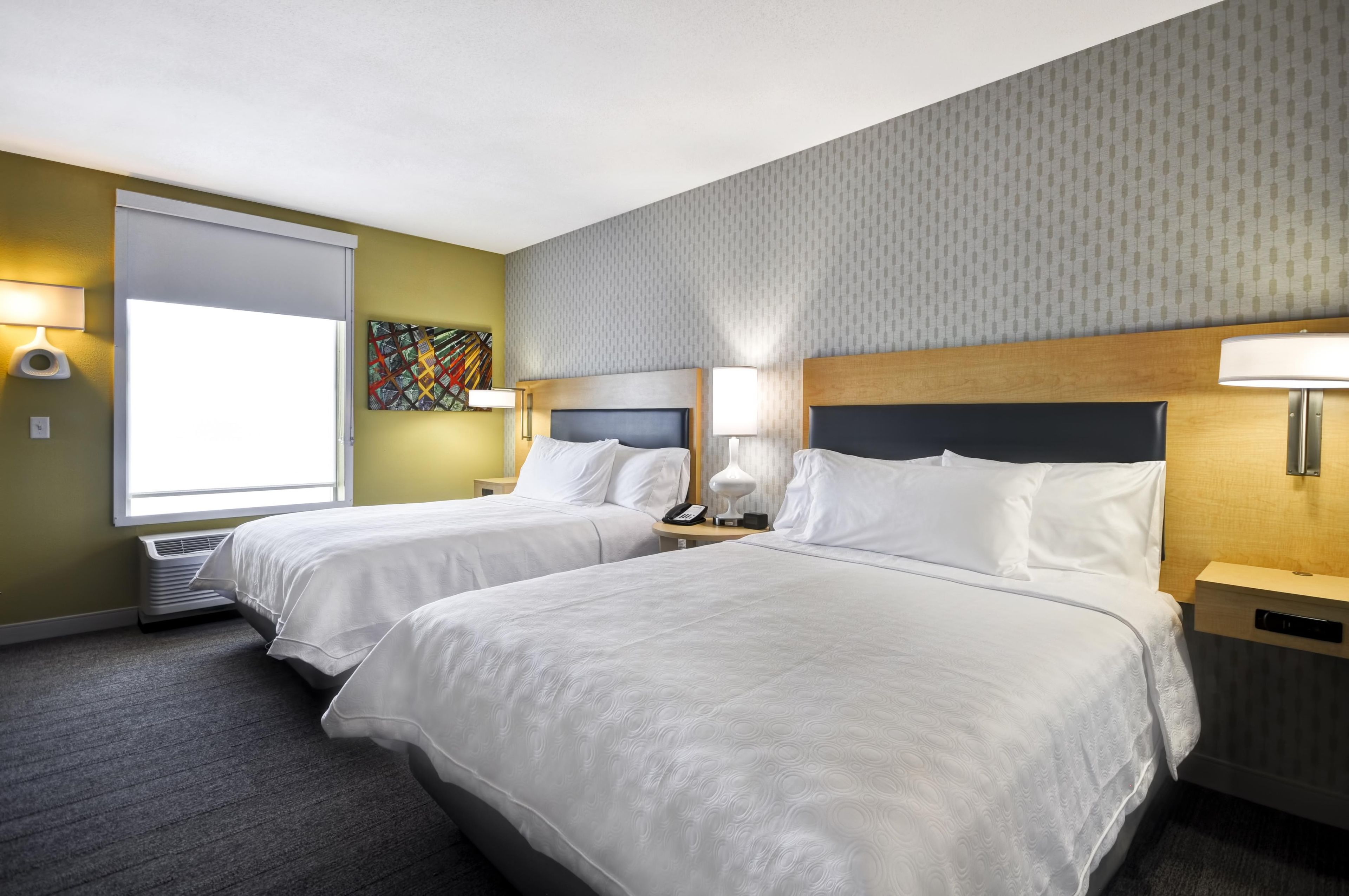A hotel room with two beds, a large window, a painting, and a patterned wall.