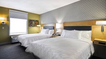 A hotel room with two beds, a large window, a painting, and a patterned wall.