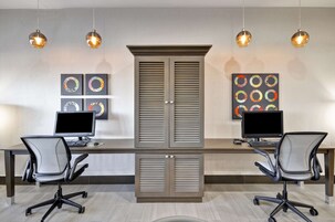 Un espacio de oficina moderno con dos escritorios, dos sillas de oficina y un mueble alto con puertas empaneladas.