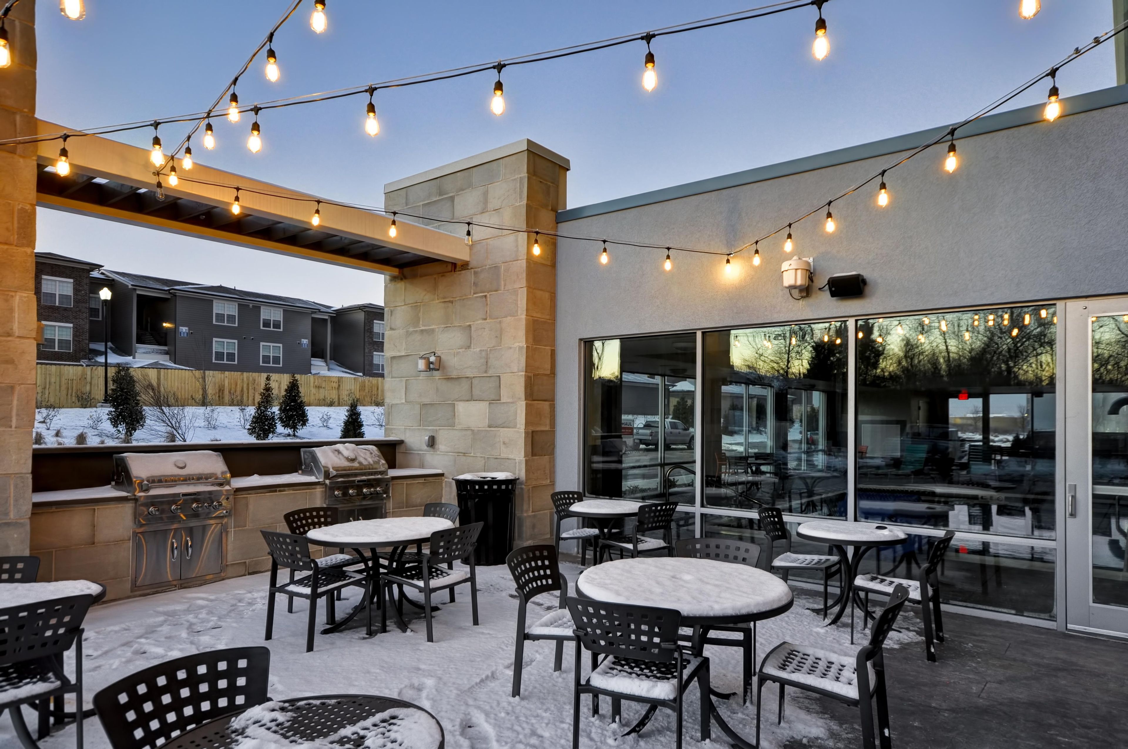 An outdoor patio area with string lights, outdoor seating, and a barbecue grill.