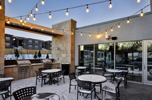 Un patio al aire libre con luces colgantes, asientos exteriores y una parrilla.