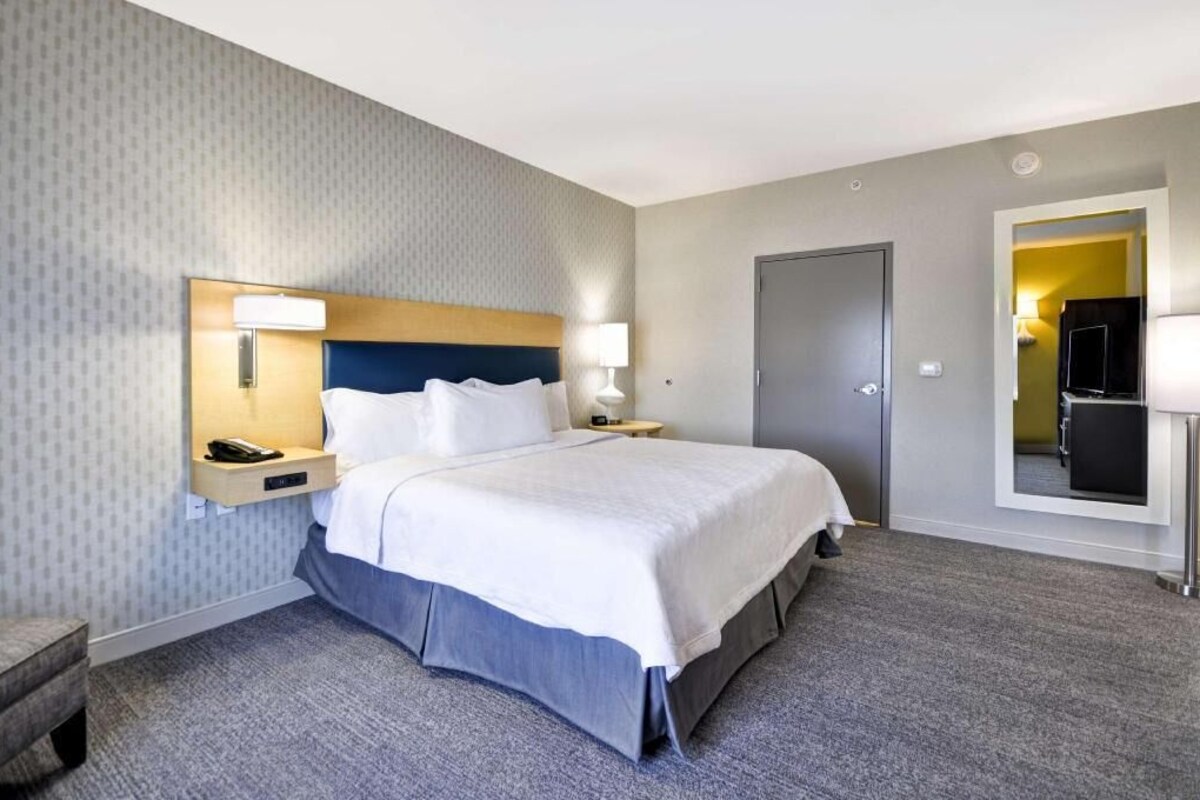 A hotel room with a bed, bedside tables, a lamp, a telephone, a door, and a mirror.