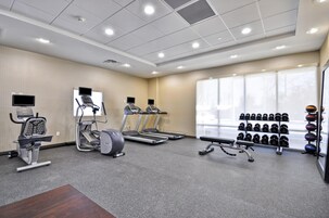 Un gimnasio con cintas de correr, elíptica, banco de pesas y una barra de mancuernas.