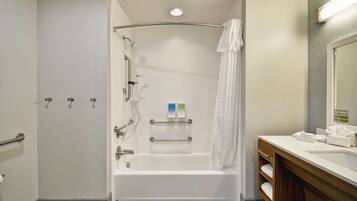 A modern bathroom with a bathtub, grab bars, a shower curtain, and a vanity with a mirror.