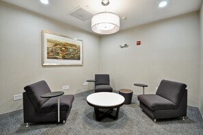 A conference room with a round table, four grey chairs, a framed cityscape painting, and ceiling lights.