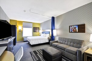 Una habitación de hotel con cama, sofá, televisión, escritorio y ventana.