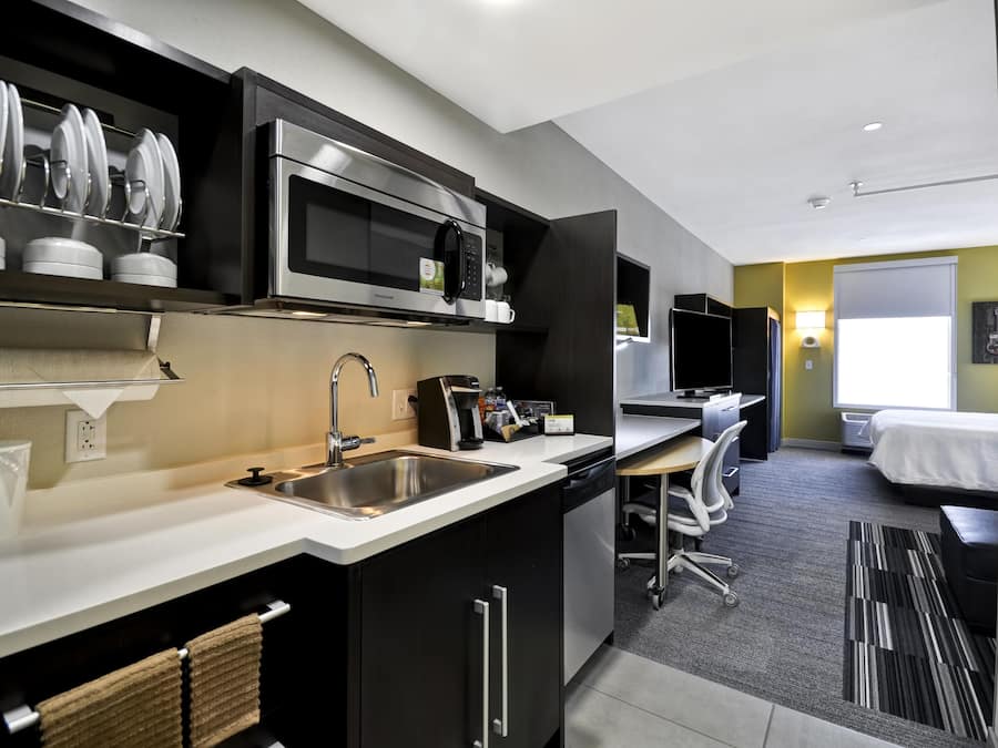 A modern kitchen with a microwave, sink, and coffee maker. There is a small dining area with a table and chairs.