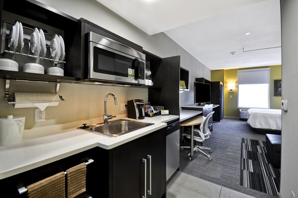 A modern kitchen with a microwave, sink, and coffee maker. There is a small dining area with a table and chairs.