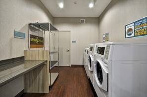 A laundry facility with a spin cycle machine, a front desk sign, and a wall-mounted vent.