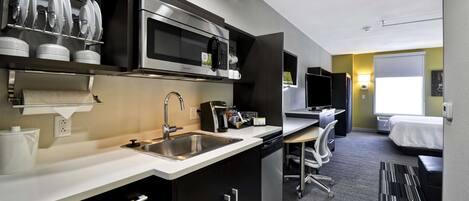 Una cocina moderna con electrodomésticos de acero inoxidable, un lavamanos y una encimera. Hay una zona de comedor con una mesa y sillas, y una cama al fondo.