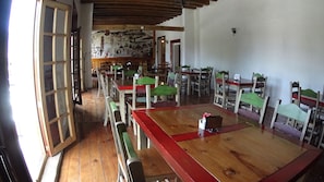Un comedor con mesas y sillas de madera, un mural en la pared y un techo de madera.