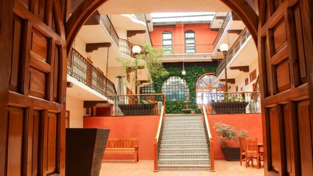 A spacious atrium with a central staircase, wooden doors, and a balcony with plants. - Hotel Santa Fe (Tlatlauquitepec)
