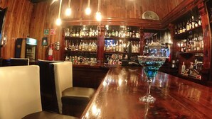 A bar with wooden walls, multiple liquor bottles, and bar stools. - Hotel Santa Fe (Tlatlauquitepec)