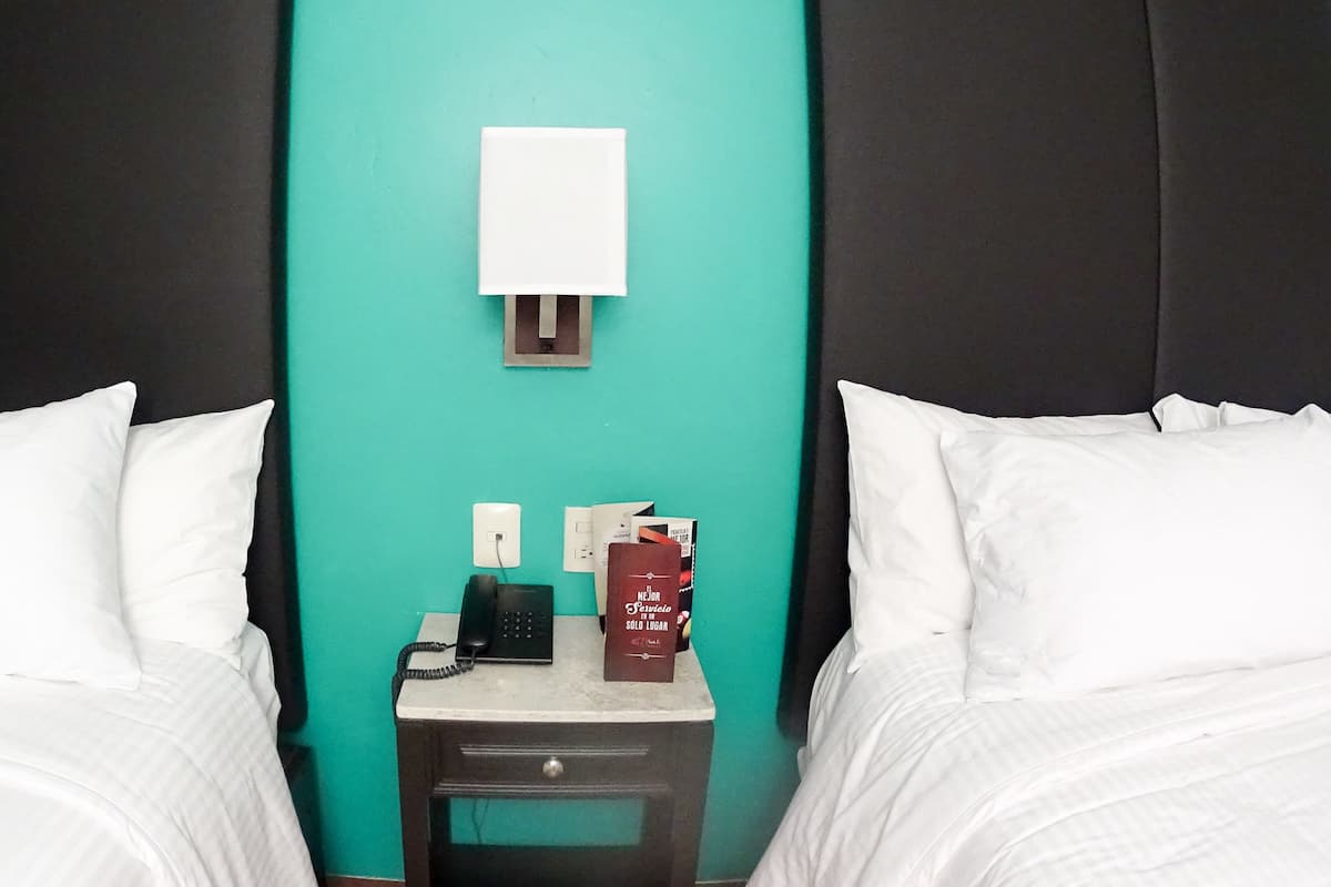 Una habitación de hotel con dos camas, una mesita de noche, un teléfono y un libro.