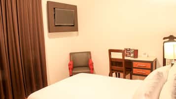 A hotel room with a bed, a desk, a chair, a TV mounted on the wall, and a lamp.
