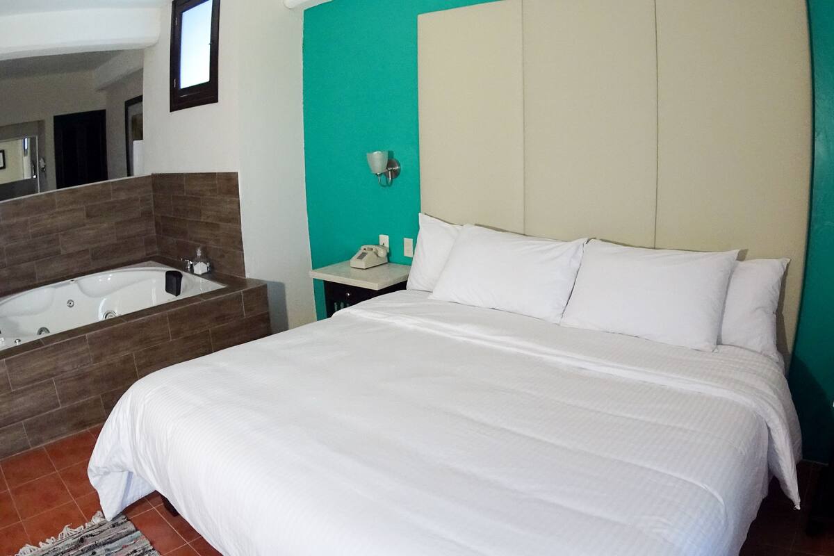 Una habitación de hotel con una cama grande, un baño separado con bañera y una mesita de noche pequeña.