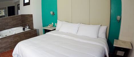 Ett hotellrum med en stor säng, ett separat badrum med badkar och ett litet nattduksbord.