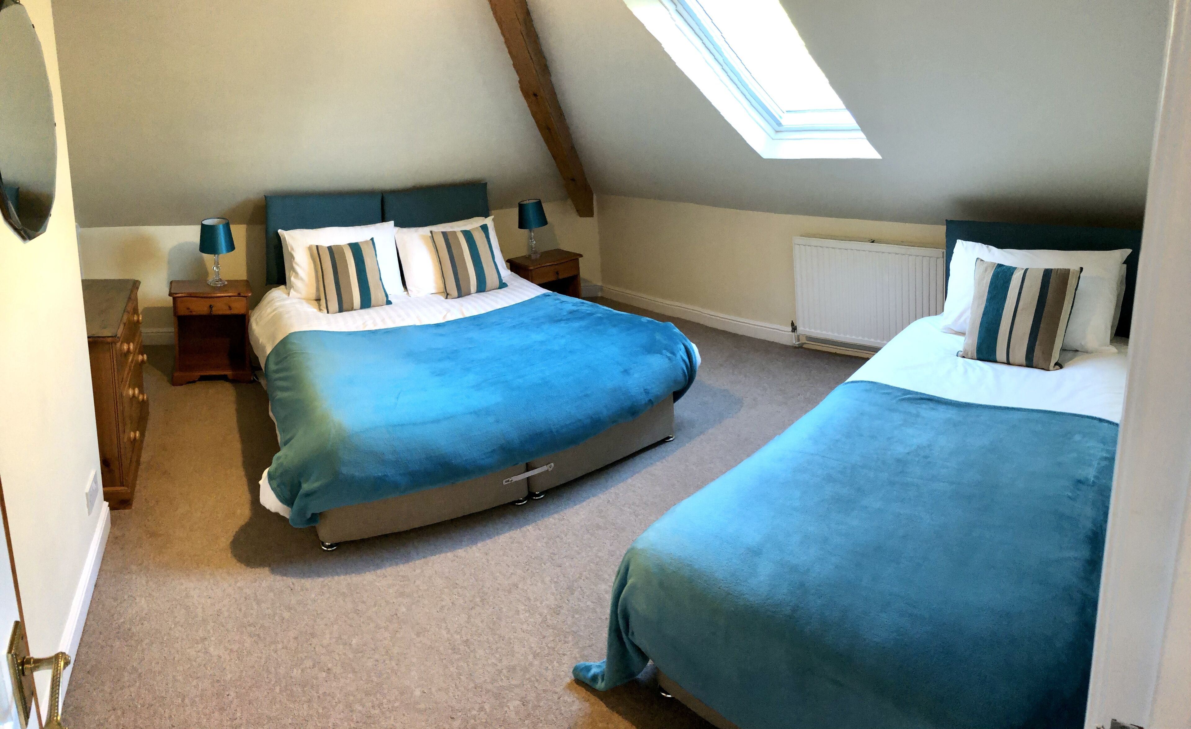 Ein Schlafzimmer mit zwei Betten, einem Oberlicht, einer Holzkommode und einer Heizung.