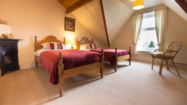 A bedroom with two wooden beds, a fireplace, a window with curtains, and a wooden ceiling. - Spacious stylish house for group stays in  beautiful Buxton, pet friendly.   (Buxton)