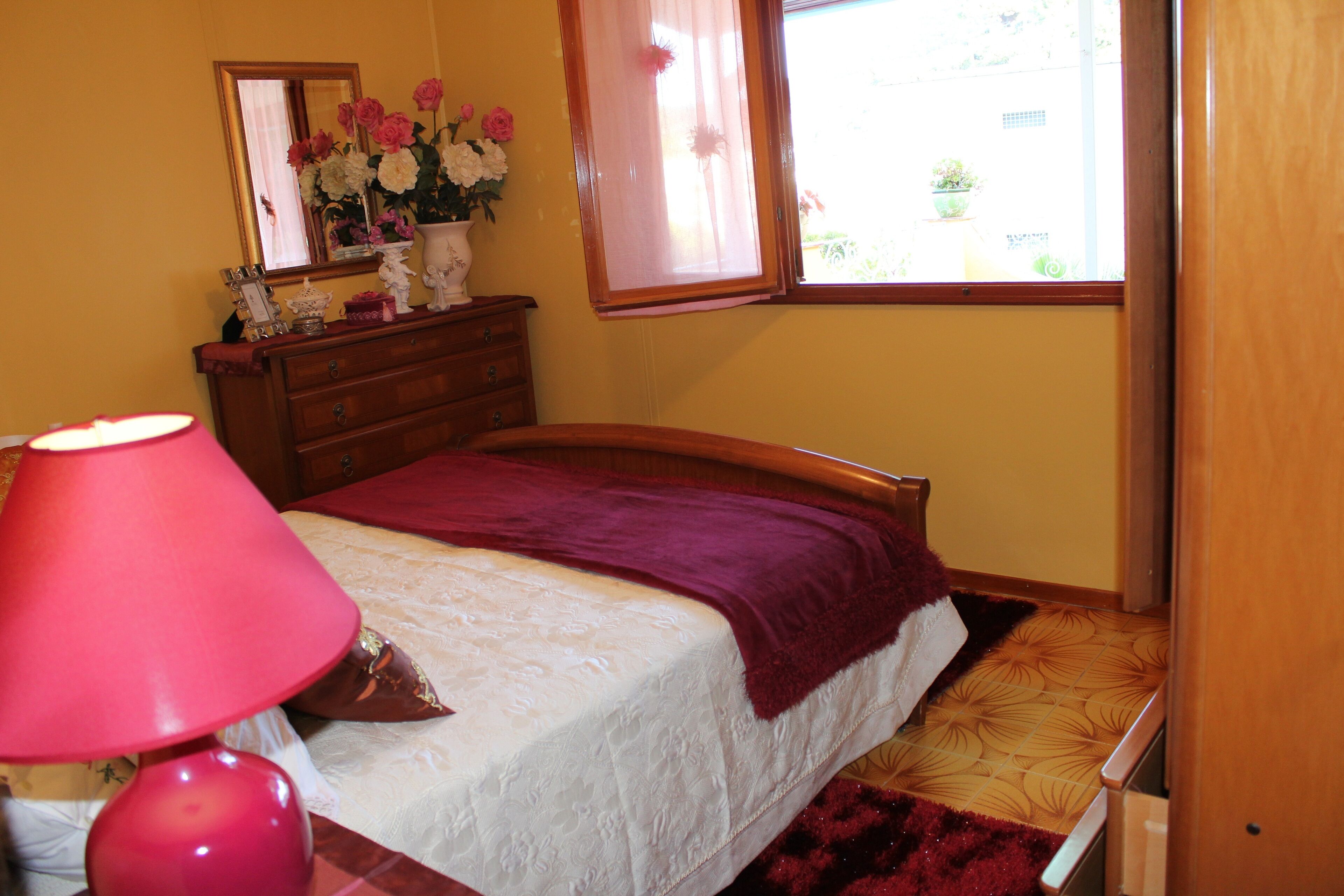 A bedroom with a bed, a dresser, a mirror, and a window with a view of the outside.