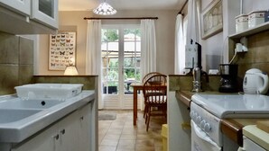 Een keuken met een eettafel, stoelen, een kroonluchter en een raam met gordijnen.