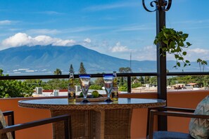 Terraço com vista para montanha, mesa com duas taças e uma garrafa, e mobiliário de vime.