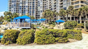 A high-rise hotel with multiple balconies and a pool area with blue umbrellas.