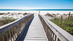 A wooden boardwalk leading to a beach with sand dunes and a clear blue sky.