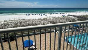 Blick auf einen Strand vom Balkon aus, mit Pool und Liegestühlen.