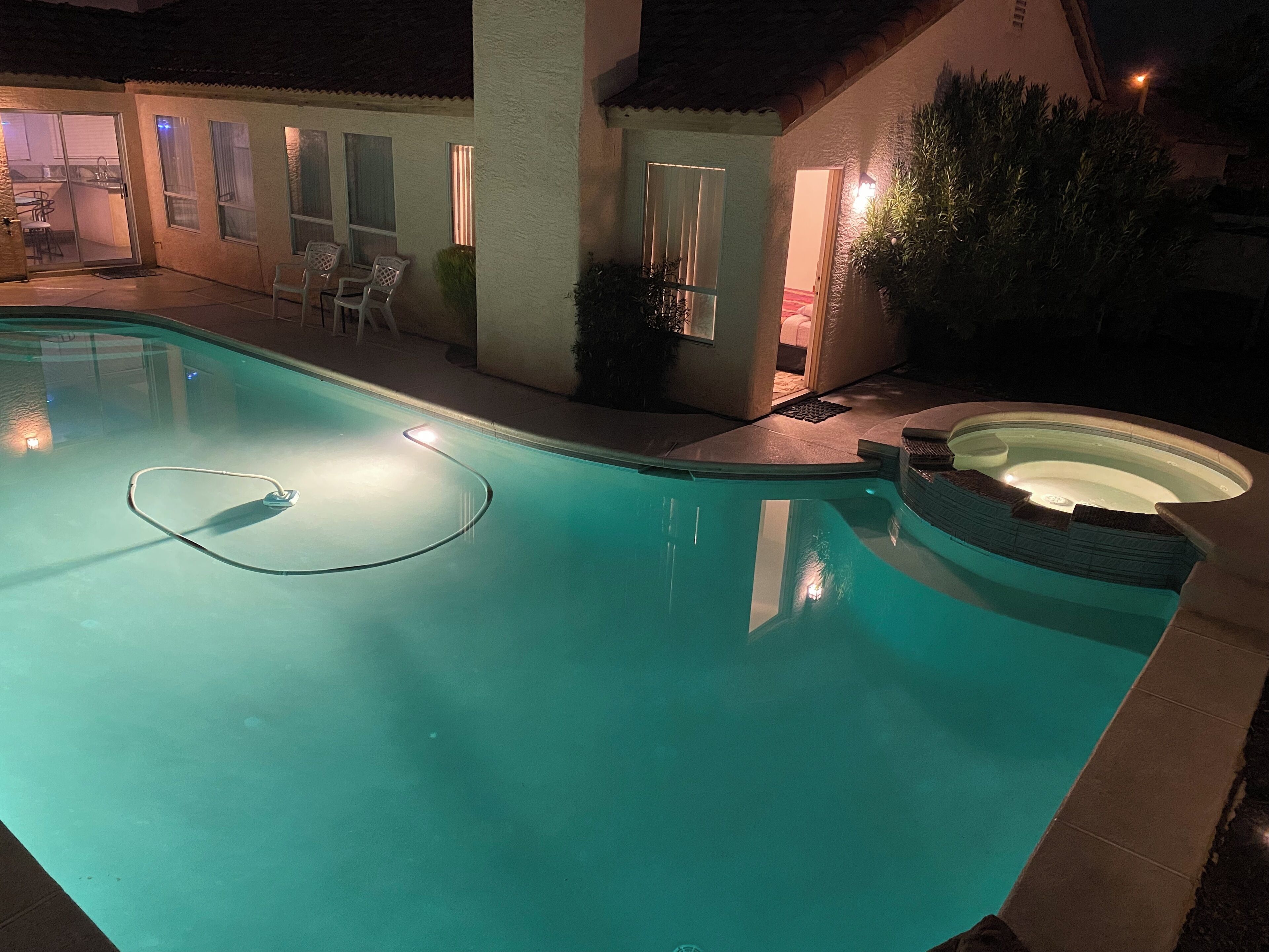 Piscina com hidromassagem, rodeada por um terraço com cadeiras e um pequeno jardim.