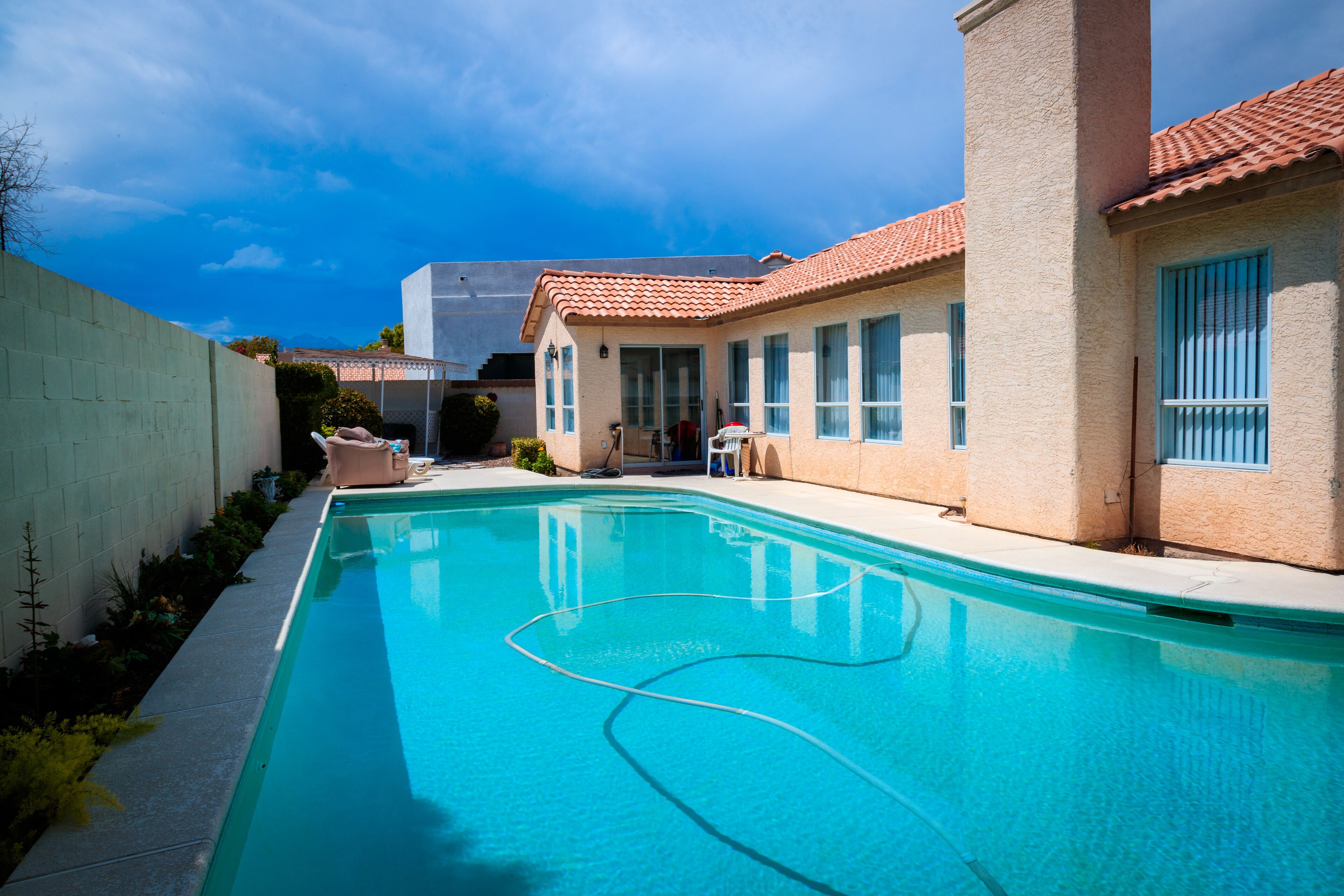 Una piscina con una línea de agua azul cristalina, rodeada por un edificio color beige con tejado de tejas y ventanas.