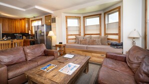A cozy living room with a brown leather sofa, a wooden coffee table with magazines, and a window seat with cushions.