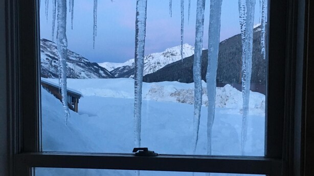 A window with a view of a snowy landscape and icicles hanging from the window frame.