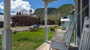A porch with white chairs, a brick building, and a mountain in the background.
