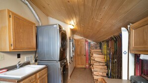 A narrow kitchen with wooden cabinets, a built-in washing machine, and a row of skis against the wall.