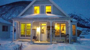 A two-story house with a covered porch and large windows, surrounded by snow.