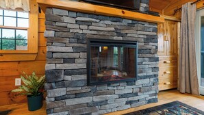 A stone fireplace with a TV above it, wooden walls, and a potted plant.