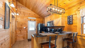 A wooden cabin interior with a kitchen area featuring a refrigerator, microwave, and bar stools.