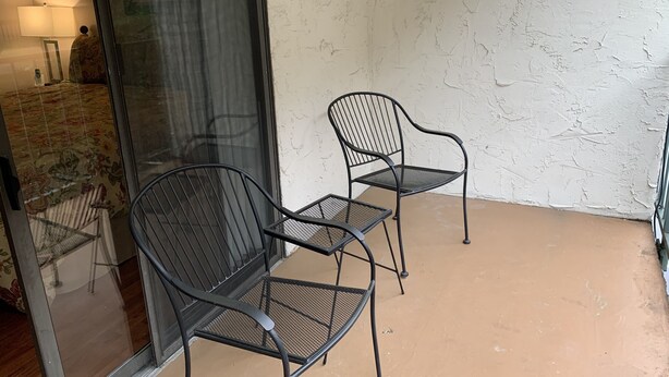 A small patio with two metal chairs and a table, a glass door, and a textured wall.
