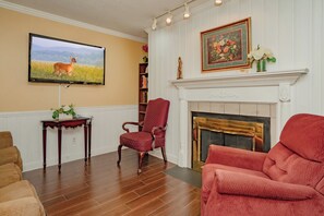 Una sala de estar con chimenea, un televisor montado en la pared y un sillón rojo.