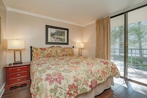 A bedroom with a floral bedspread, two bedside lamps, a nightstand, a dresser, and a framed picture on the wall. - Oak Square Rentals 110 is a lovely condo with bunk beds in downtown (Gatlinburg)