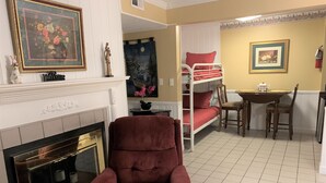 A living room with a fireplace, a red armchair, a bunk bed, and a dining table.