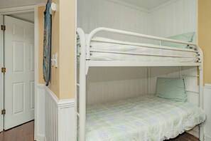 Un lit superposé avec un matelas vert et un seul oreiller, dans une pièce aux murs blancs et dotée d’une porte.