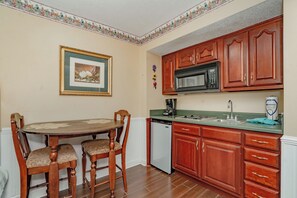 A kitchen with wooden cabinets, a microwave, a dishwasher, a table with chairs, and a framed picture on the wall. - Oak Square Rentals 110 is a lovely condo with bunk beds in downtown (Gatlinburg)