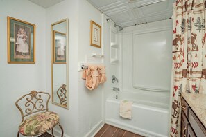A bathroom with a bathtub, a mirror, a framed picture, a bathrobe, and a chair. - Oak Square Rentals 110 is a lovely condo with bunk beds in downtown (Gatlinburg)