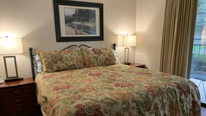 A bedroom with a floral bedspread, two bedside lamps, a nightstand with a mirror, and a framed picture on the wall.