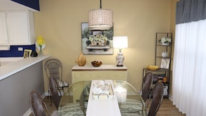 A dining area with a glass table, chairs, a white table runner, a decorative lamp, and a shelf with flowers. - Islander Bch Resort 2004 by AJH Rentals FREE BEACH SERVICE+TICKETS! $349/Day (Fort Walton Beach)