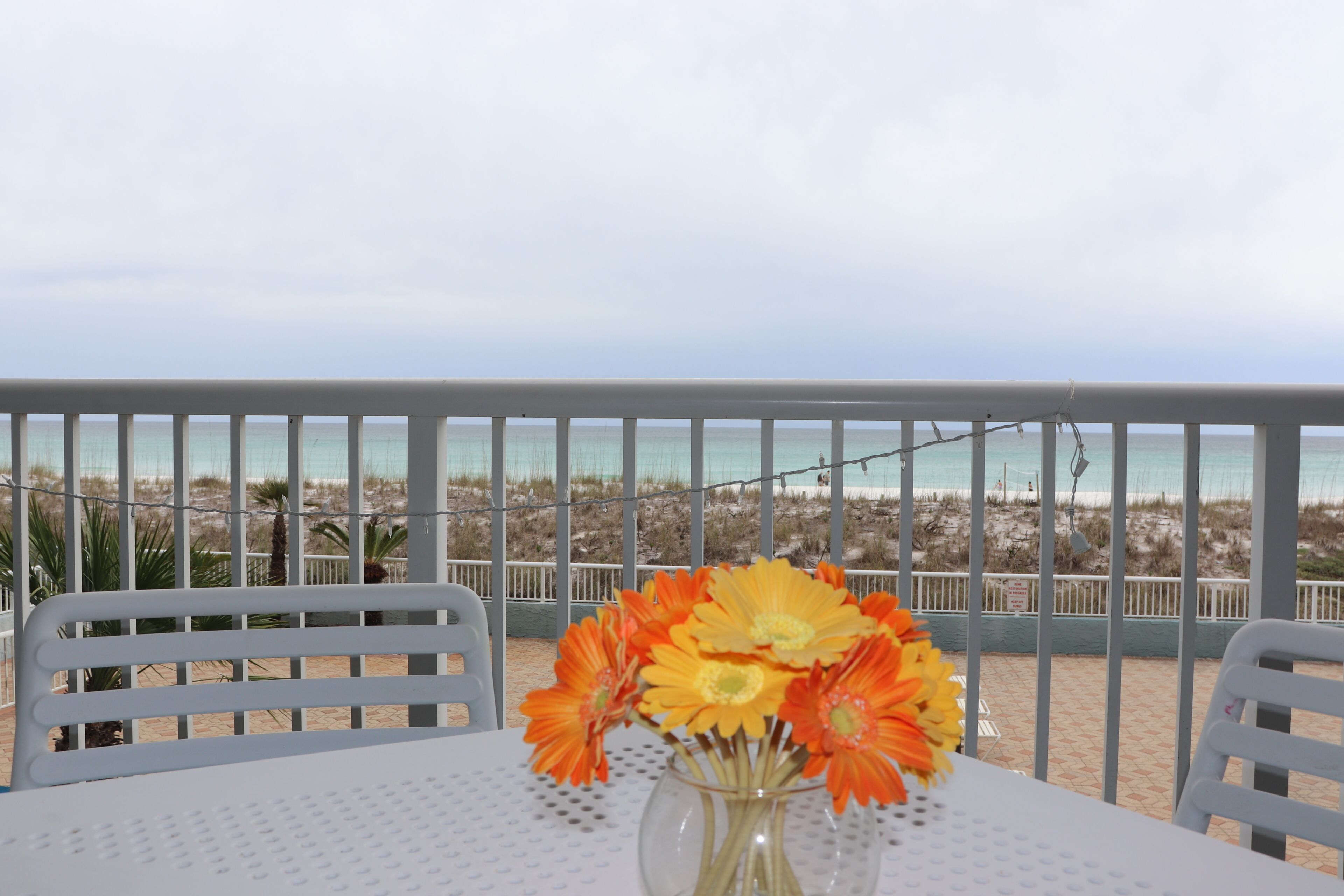 Ein Tisch mit Blumen in einer Vase, weiße Stühle und Blick auf den Strand.
