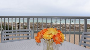 A table with a vase of flowers, white chairs, and a view of the beach. - Islander Bch Resort 2004 by AJH Rentals FREE BEACH SERVICE+TICKETS! $349/Day (Fort Walton Beach)