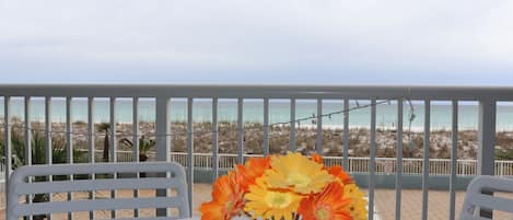 A table with a vase of flowers, white chairs, and a view of the beach.